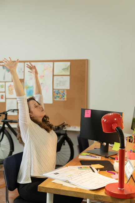 An office worker sitting at a modern desk and gently stretching their neck and shoulders during a break.